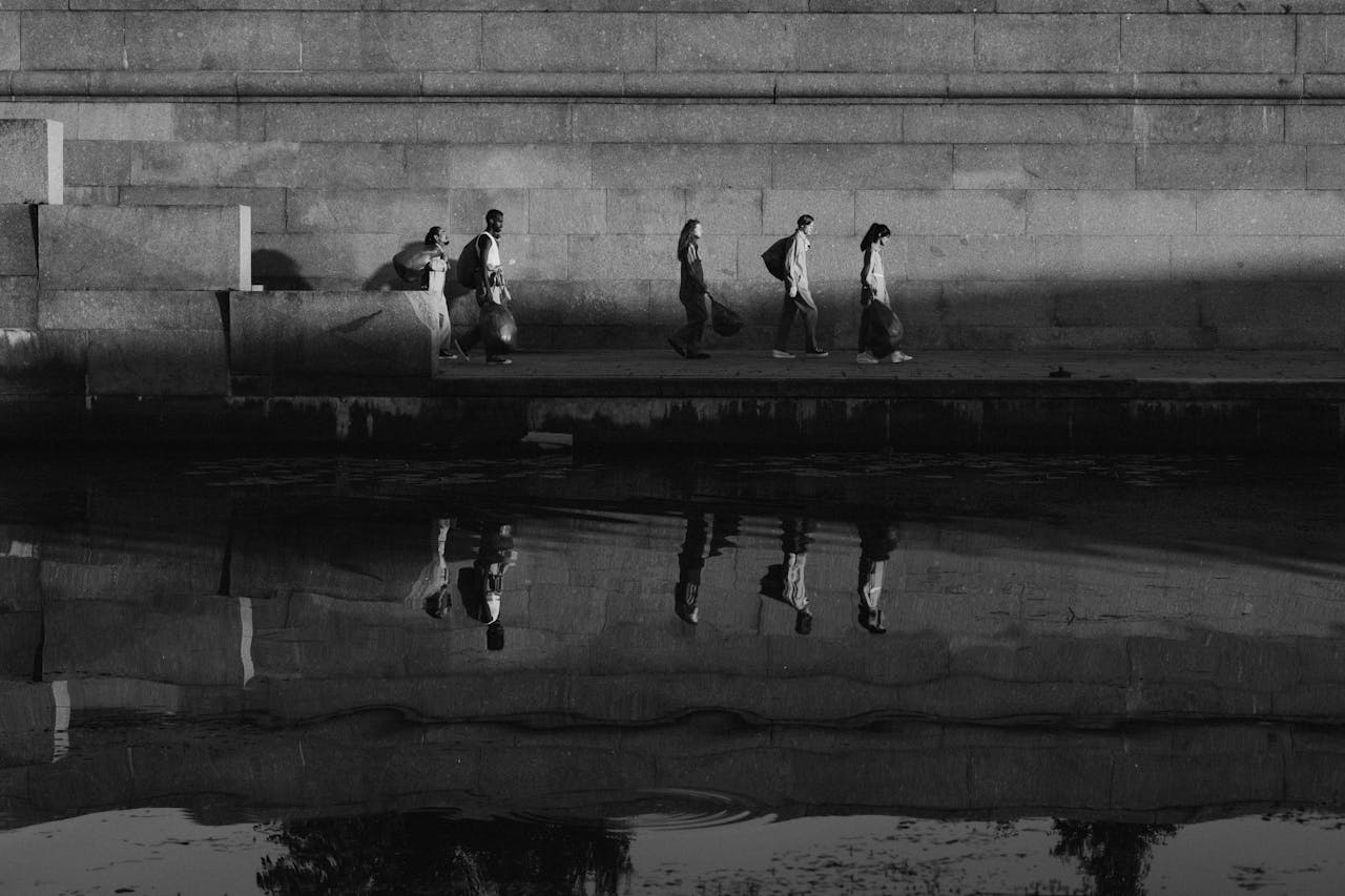 A group of people walking along a canal with reflections on the water, participating in community service.